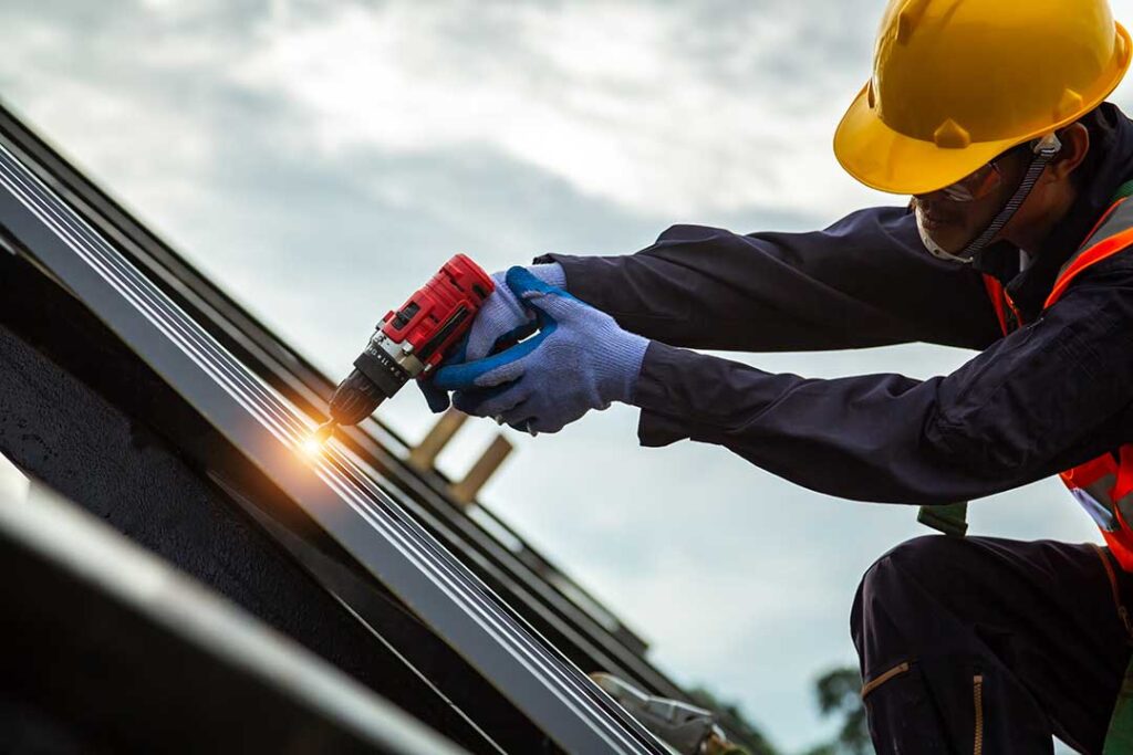 Homeowner inspecting a rain gutter and downspout beneath a shingled roof in autumn.
