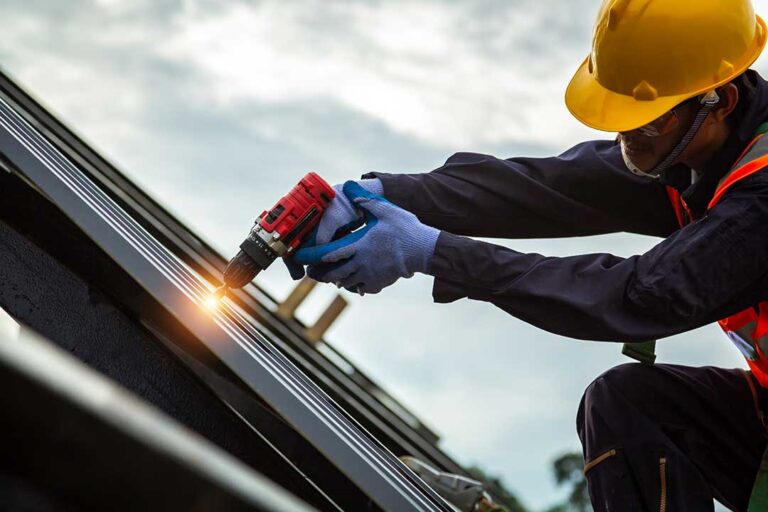 Homeowner inspecting a rain gutter and downspout beneath a shingled roof in autumn.